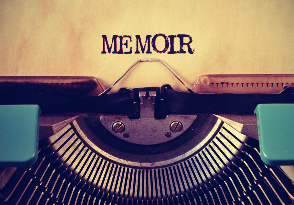 Turquoise typewriter with the typed words memoir vs autobiography on parchment paper